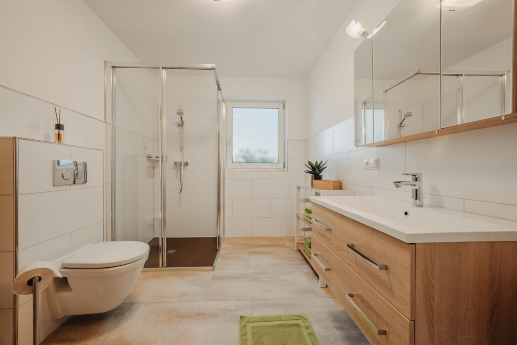 helles modernes Bad mit beigen Bodenfließen, weißen Wandfließen, Toilette, Glasdusche und Waschbecken