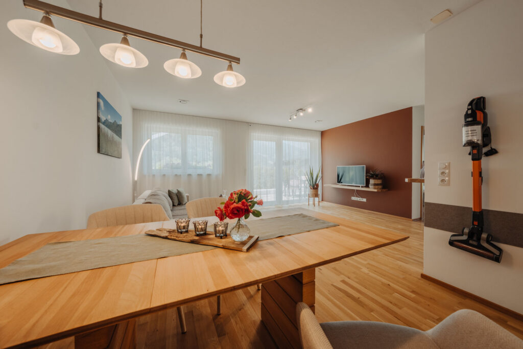 Blick von Küche auf modernen Holzesstisch, modernes Sofa und Fensterfront mit Balkon